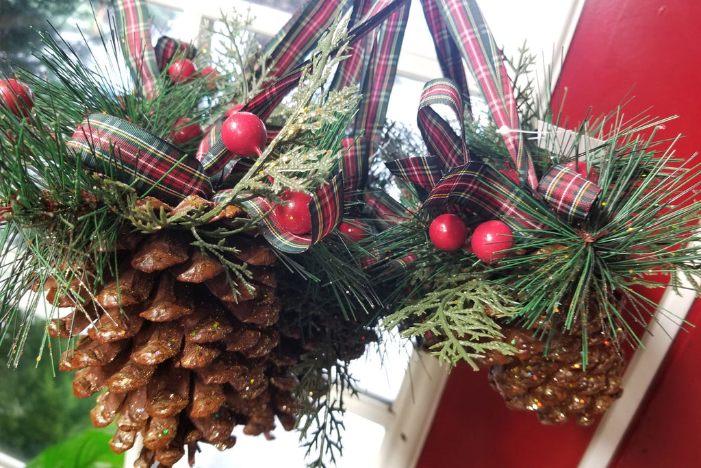 decorated large greenery pine cones with flanel ribbon, berries, and glitter